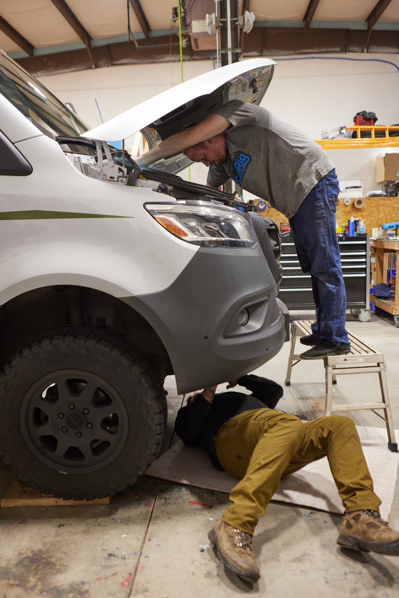 Two people working on the engine of a Sprinter van